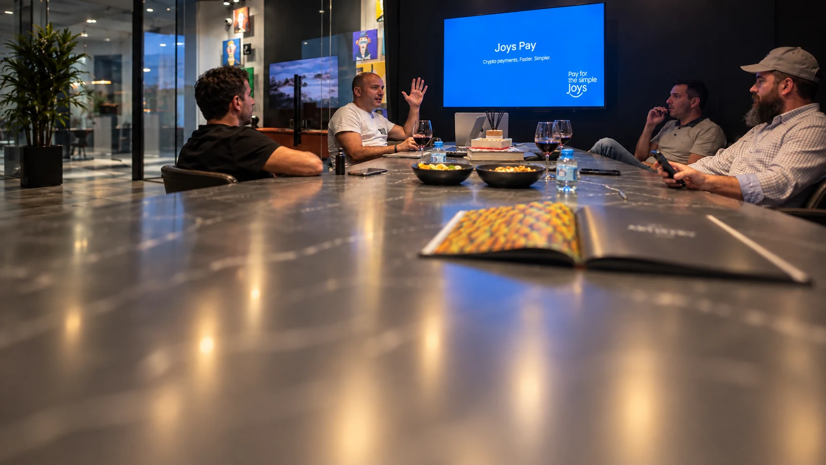 The original colleagues in conversation around their meeting table with the Joys Pay screen behind them.